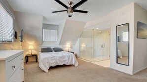 Camera da letto con un letto, lampade sui comodini, una ventola a soffitto, cabina doccia in vetro e un grande specchio.