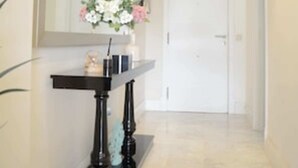 Ein Flur mit einem Spiegel, einem kleinen Tisch mit Blumen in einer Vase und einer weißen Tür am Ende.
