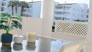Ein Balkon mit Glastisch, weißen Stühlen, einem Blumentopf und Blick auf weiße Gebäude und Palmen.