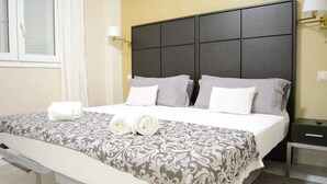 Ein Hotelzimmer mit einem großen Bett, einem Nachttisch, einer Bank und einem Fenster mit Vorhängen.