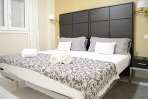 Ein Hotelzimmer mit einem großen Bett, einem Nachttisch, einer Bank und einem Fenster mit Vorhängen.