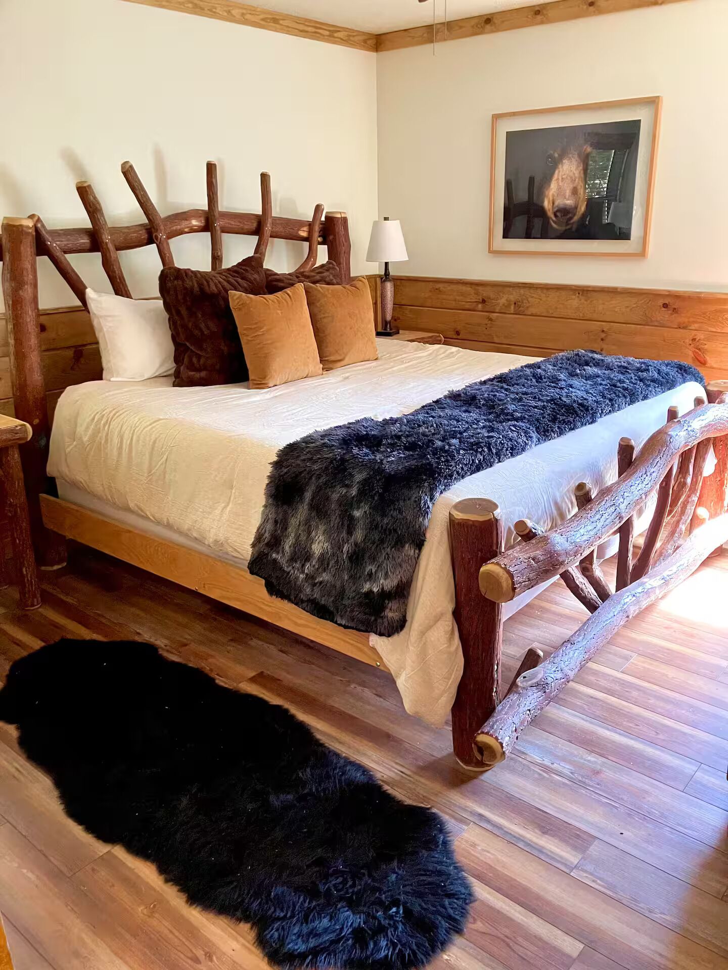 Una cama de madera con cabecera, un felpudo negro y un cuadro enmarcado en la pared.
