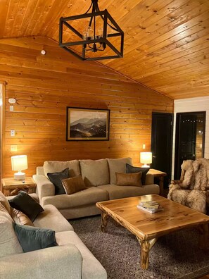 A cozy room with wooden walls, a sofa, a coffee table, and a fur chair. - Fox Hollow Hideaway - Cabin (Gatlinburg)