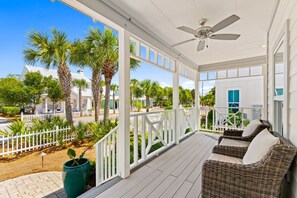 A covered porch with wicker furniture, a ceiling fan, and a view of palm trees and buildings. - 🌞Sun & Moon at 30A – Two Homes | Walk to Beach | Sleeps 14🌙 (Santa Rosa Beach)