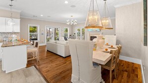 Eine moderne Küche mit weißen Schränken, ein Essbereich mit Holztisch und ein Wohnzimmer mit Sofa.
