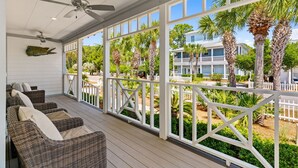A covered porch with wicker furniture, a ceiling fan, and a view of a residential area with palm trees and a blue building. - 🌅 Golden Sun – Stylish 30A Beach Retreat | Walk to Gulf | Sleeps 8 🏖️ (Santa Rosa Beach)