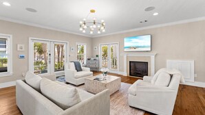 A spacious living room with a fireplace, a large TV, and a view of the outdoors through the windows. - 🌅 Golden Sun – Stylish 30A Beach Retreat | Walk to Gulf | Sleeps 8 🏖️ (Santa Rosa Beach)