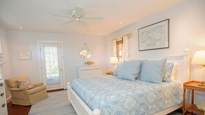 Ein Schlafzimmer mit einem Bett, einem Sessel, einem Nachttisch, einer Lampe, einem Deckenventilator und einer Tür.