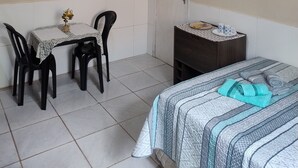 A room with a bed, a small table with chairs, a desk, and a door.