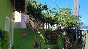 Um pátio com parede verde, um banco de madeira, plantas em vasos e um candeeiro suspenso.