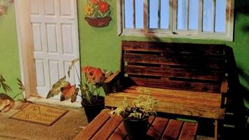 Um banco de madeira, uma mesa, um vaso de planta, uma porta e uma janela com vista.