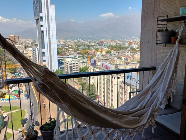 Eine Hängematte auf einem Balkon mit Blick auf eine Stadtlandschaft, im Hintergrund Gebäude und Berge.
