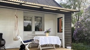 Een houten terras met een tafel en stoelen, een hangende tas en een hond die op de trap zit.