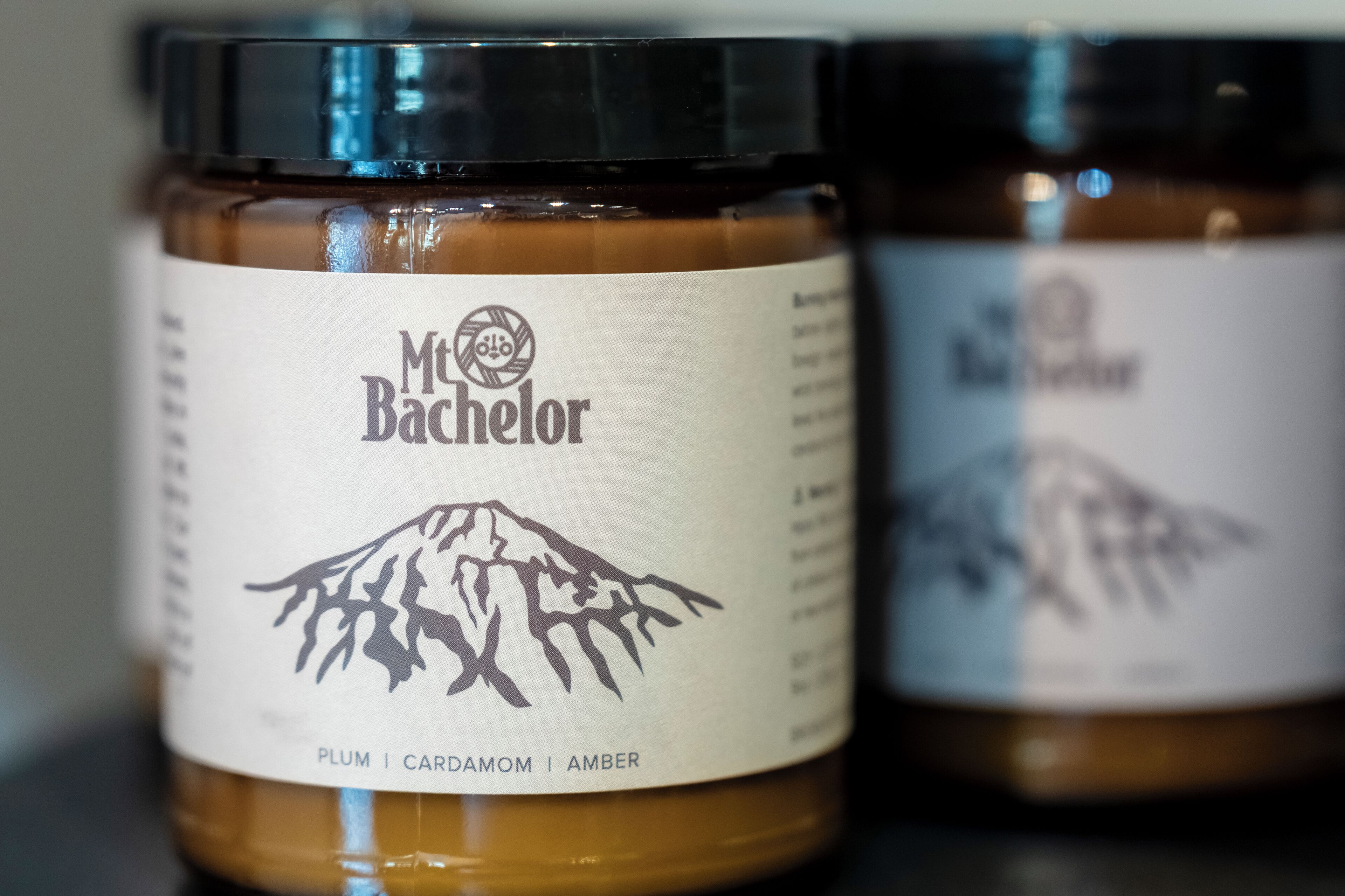 Two jars of McBacheron jam with labels indicating flavors of plum, cardamom, and amber.