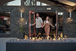 A stone facade with a glass entrance, a fire feature in the foreground, and a dining area visible through the glass. - Trailhead Lodge (Bend)
