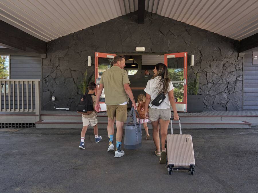 A family with a child and a suitcase at a hotel entrance with a stone facade and a red door.