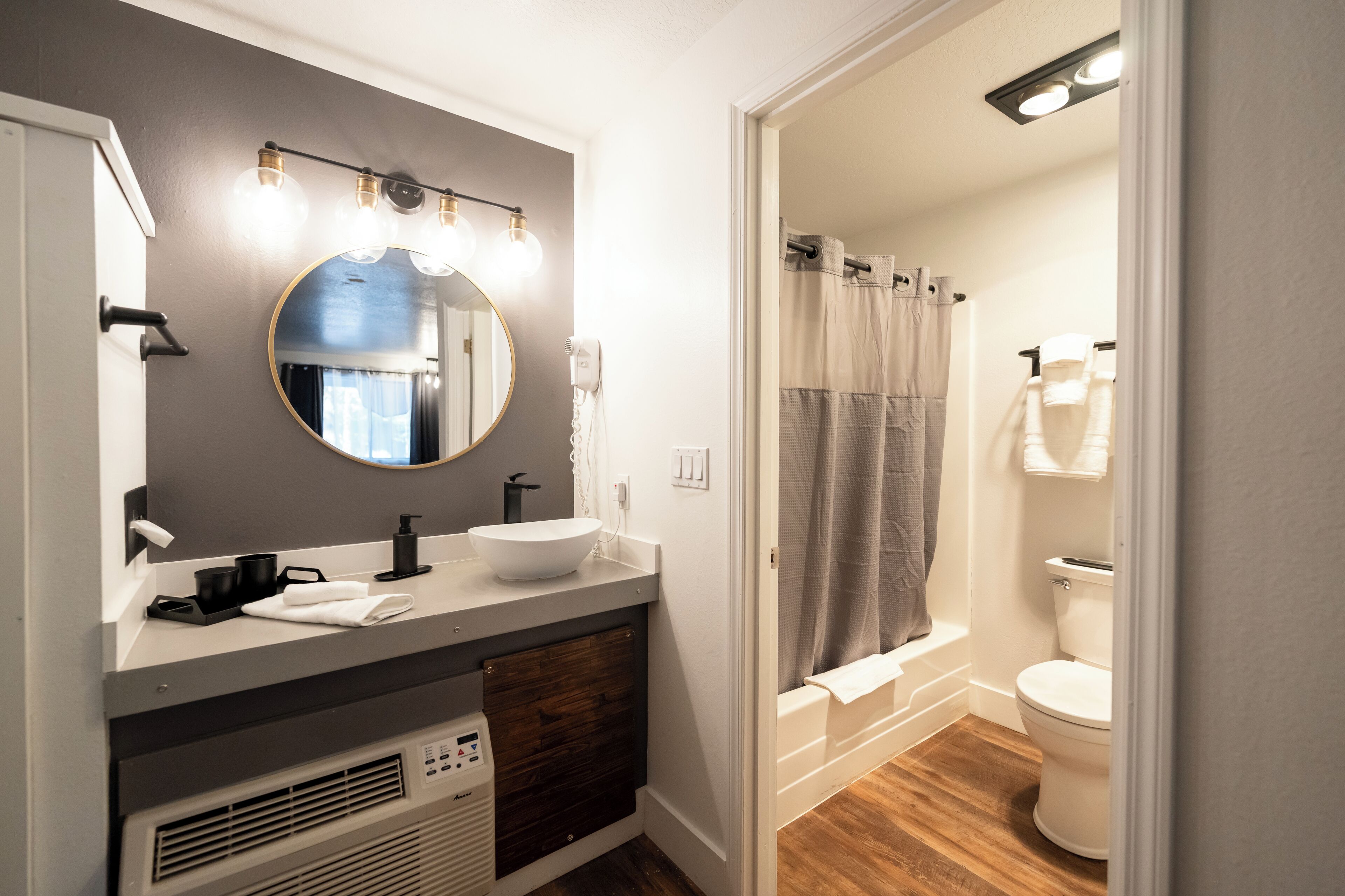 A bathroom with a vanity, sink, mirror, and a shower area.
