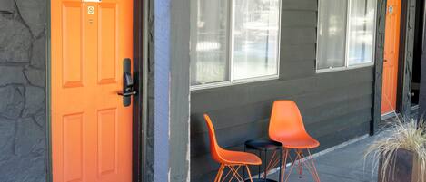 A building with two orange doors, numbered 121 and 122, and a small outdoor seating area with two orange chairs and a table.