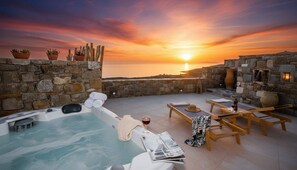 A rooftop terrace with a hot tub, lounge chairs, and a stone wall overlooking the sea during sunset. - Suite With Jacuzzi & Sea View (Mykonos)