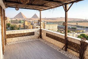 A balcony with a view of the pyramids, stone walls, and a thatched roof. - Luxury panoramic GEM and Pyramids view apartment (Giza Governorate)
