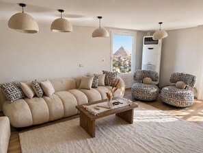 A living room with a sofa, two patterned chairs, a coffee table, and hanging pendant lights. - Luxury panoramic GEM and Pyramids view apartment (Giza Governorate)
