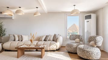 Ein modernes Wohnzimmer mit einer Couch, Hocker, einem Couchtisch, Pendelleuchten und Blick auf eine Pyramide durch ein Fenster.