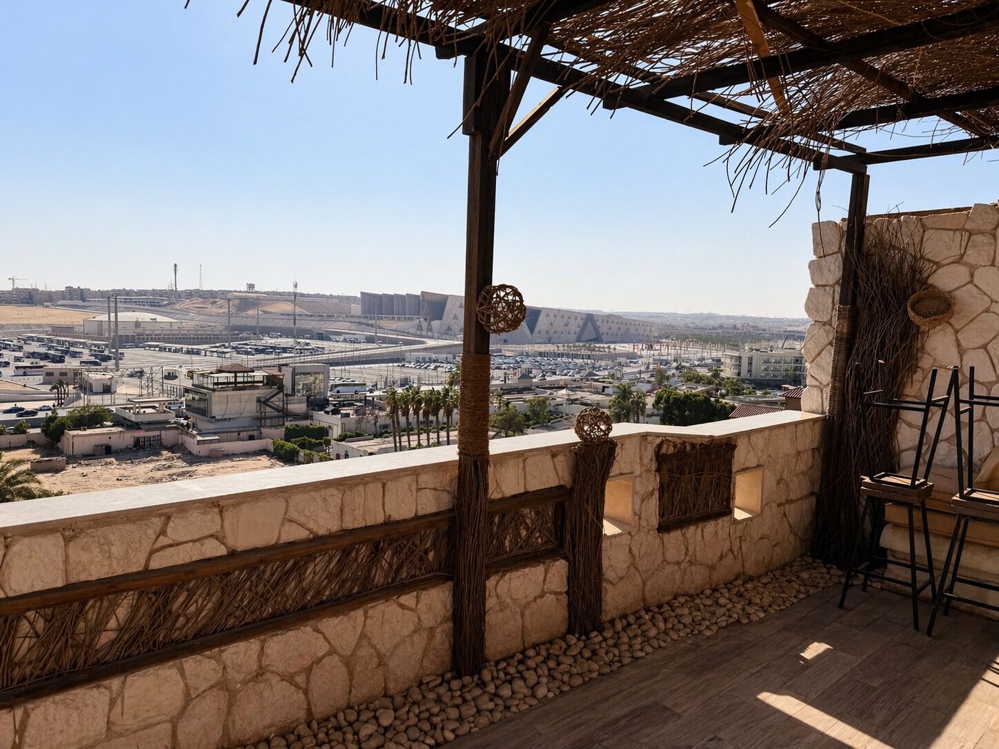 A terrace with a stone wall, a thatched roof, and a view of an industrial area.