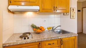Eine Küche mit Holdekor-Schränken, einer Arbeitsplatte aus Granit, einem eingebauten Herd, einer Spüle und einer Obstschale mit Orangen und Ananas.