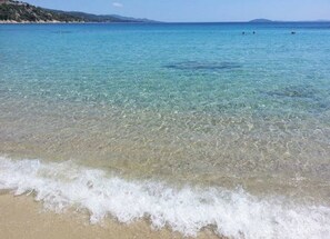 Ein Strand mit klarem Wasser, sandigem Ufer und weit entfernten Hügeln.