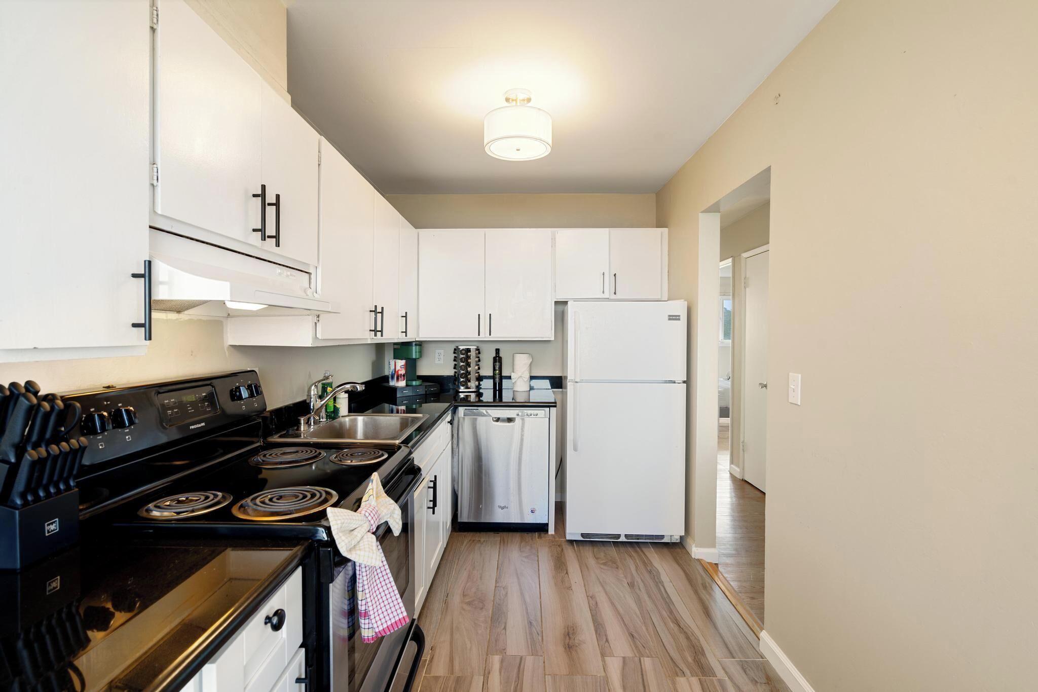 A kitchen with white cabinets, a black stove, a white refrigerator, and a wooden floor.