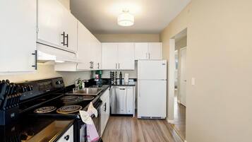 A kitchen with white cabinets, a black stove, a white refrigerator, and a wooden floor.