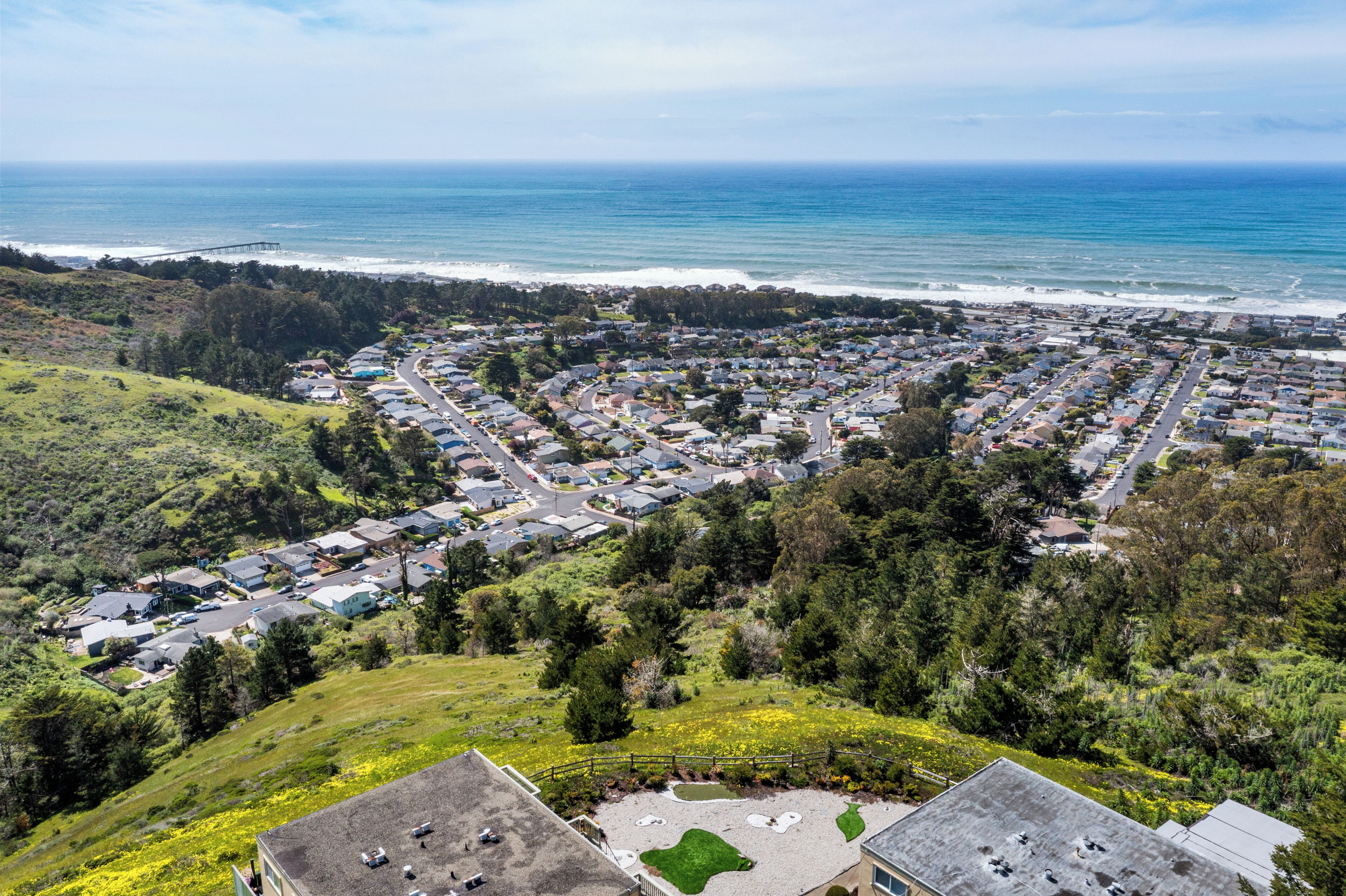 A coastal residential area with houses, a road, and a view of the ocean.