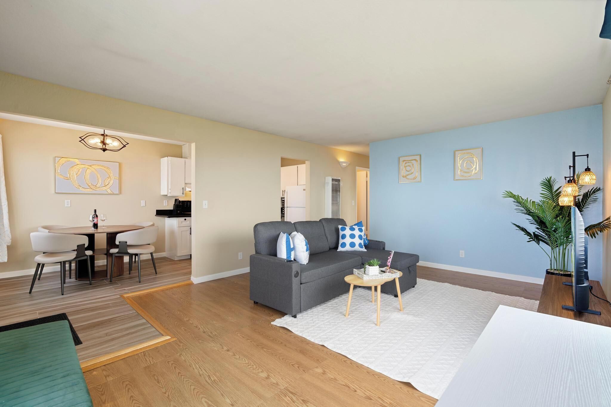 Een moderne woonkamer met een grijze bank, een eettafel en een keuken op de achtergrond.
