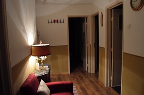 Ein Flur mit einer Lampe, einem roten Sessel, einer Uhr und einer Tür.