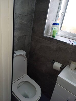 A bathroom with a toilet, a window with a shelf, and a sink. - Room-cosy Single Room Near CBS Arena and (Coventry)