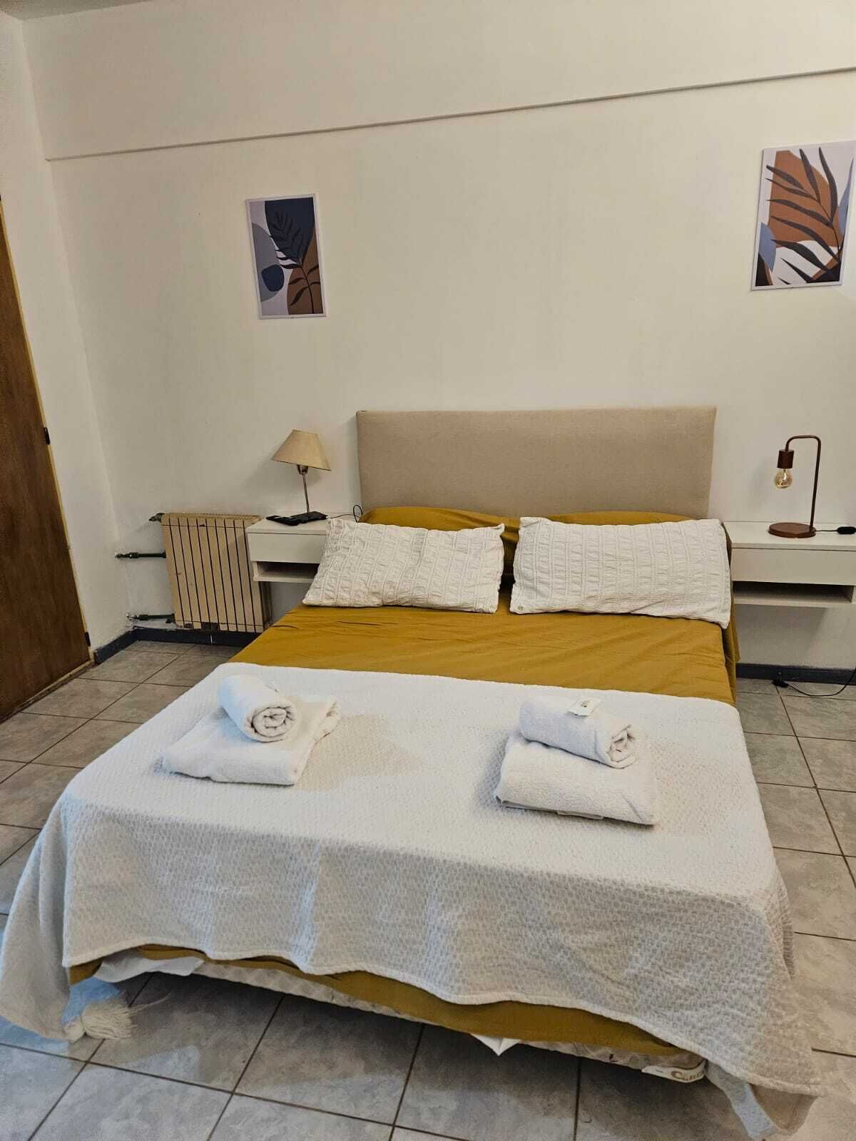 A neatly made bed with a white bedspread and two pillows, a bedside table with a lamp, and a radiator on the floor.