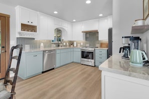 A modern kitchen with white cabinetry, a dishwasher, an oven, a coffee maker, and a blender. - Oakwood Tranquility-Peaceful 2 BR Plus Office (Atascadero)