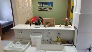 A compact kitchenette with a sink, a small trash bin, a bottle of vinegar, and a decorative umbrella.