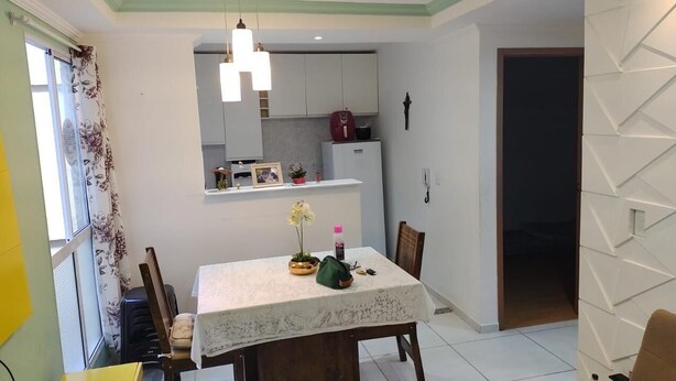 A dining area with a table, chairs, a chandelier, a refrigerator, and a kitchen counter.