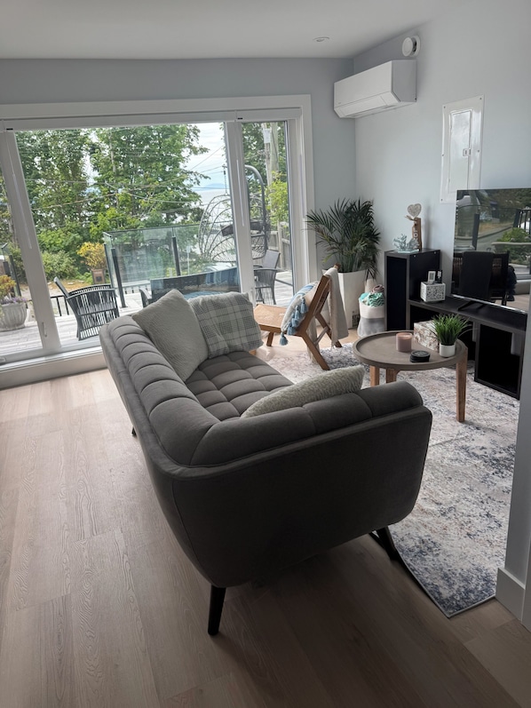 A modern living room with a sofa, a TV, and a balcony with outdoor furniture.