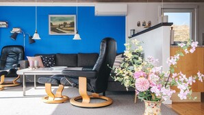 Una sala de estar moderna con una pared azul de acento, un sofá de cuero negro, una mesa de centro de madera y un jarrón floral.