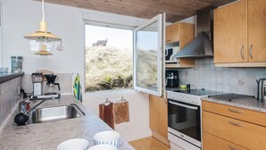Una cocina moderna con armarios de madera, horno empotrado, cafetera y ventana con vistas al exterior.