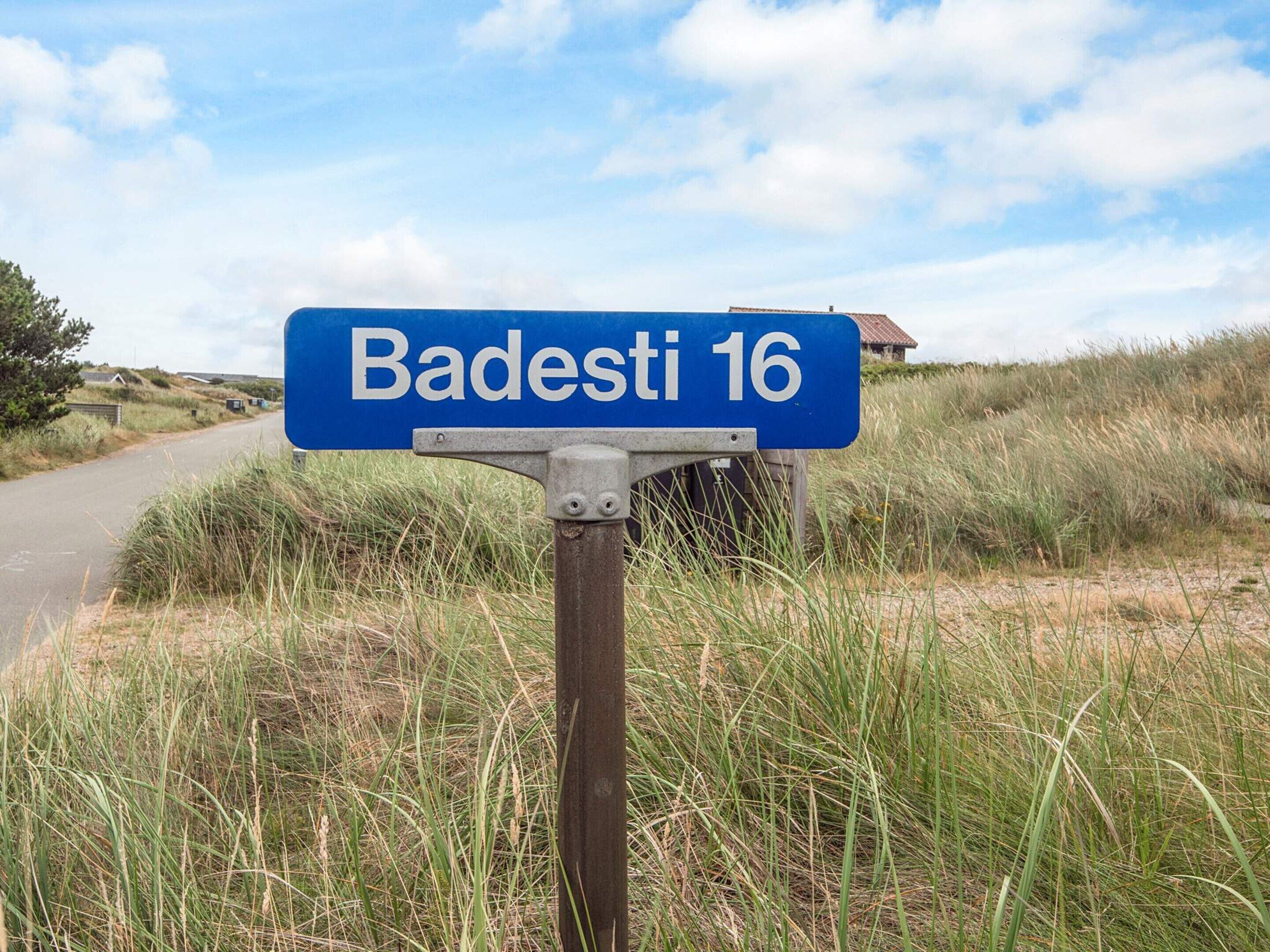A blue street sign with white text reading 'Badesi 16' in a rural setting.