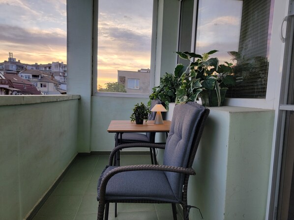 Un balcon avec un fauteuil en osier, une petite table avec une lampe et des plantes en pot.