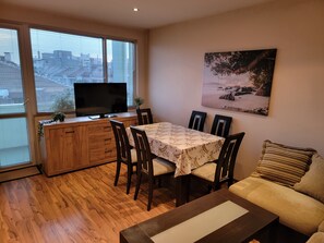 A dining area with a table, chairs, a television on a wooden cabinet, and a painting on the wall. - 
City & Beach in the Heart of Varna , Modern 2BR Apt
 (Varna)