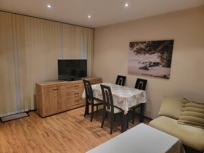 Un salon comprenant un meuble en bois, un téléviseur, une table à manger avec des chaises, un canapé et un tableau accroché au mur.