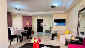 A modern living room with a black coffee table, a red vase, a sofa, a TV, and a dining area with chairs and a table. - Palmeraie fountain view (Marrakech)