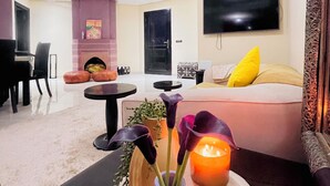 A modern living room with a sofa, a TV mounted on the wall, a fireplace, and a dining area with a table and chairs. - Palmeraie fountain view (Marrakech)