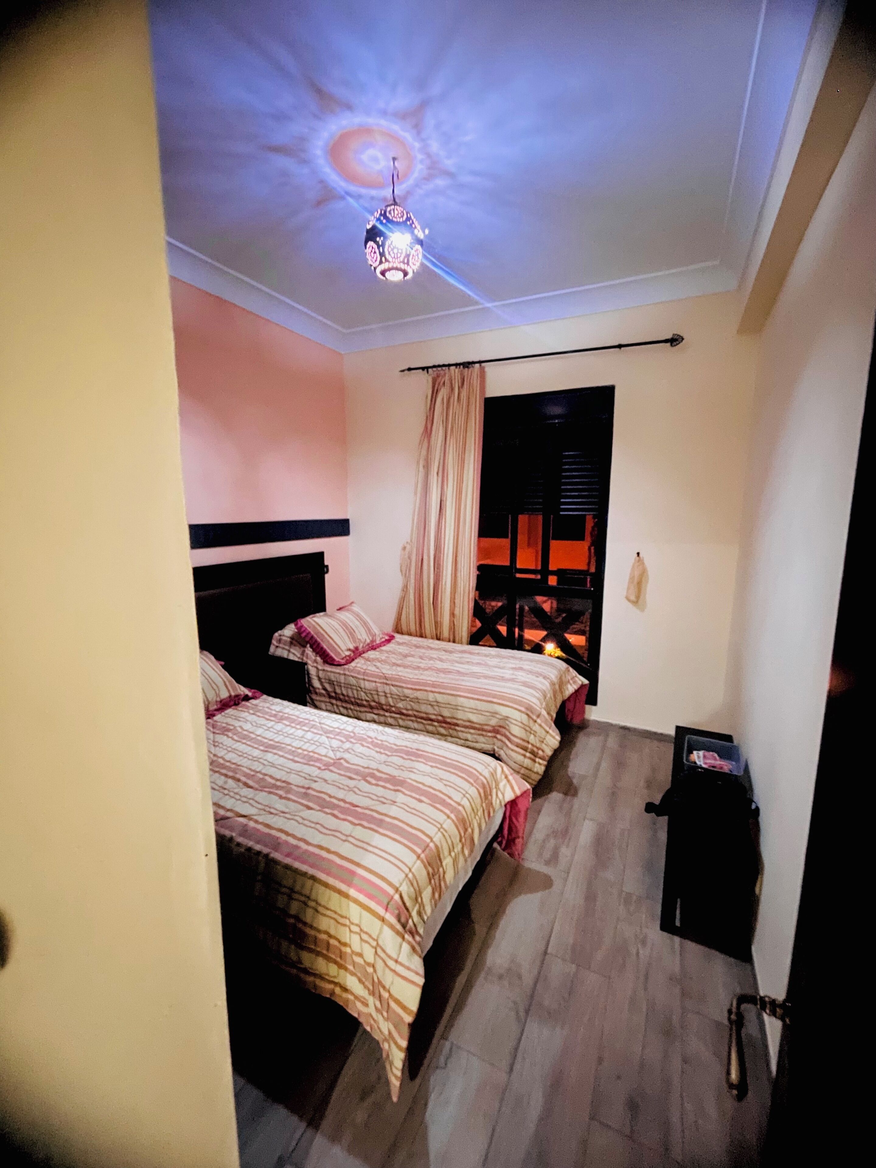 Une chambre avec deux lits, un luminaire au plafond et une petite table.