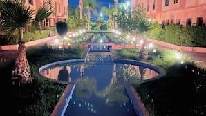 A nighttime view of a hotel with a central water feature, palm trees, and illuminated pathways. - Palmeraie fountain view (Marrakech)
